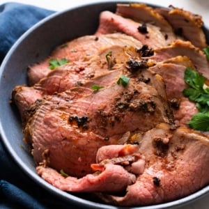 Sliced eye of round roast with au jus and parsley on a plate.