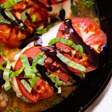 Baked caprese chicken garnished with balsamic glaze and fresh basil in a skillet.