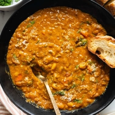 Instant pot 15 bean soup in a bowl with spoon and slice of baguette.